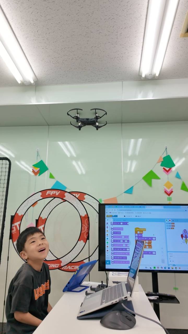 東京都荒川区西尾久の子どもドローン教室で、飛んだドローンを見上げて笑顔になる小学生
