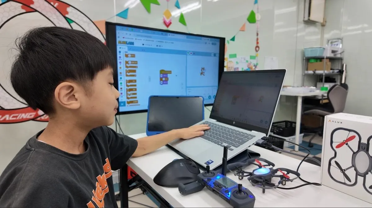 パソコンでブロックプログラミングを組み立てる小学生とドローン・送信機（荒川区西尾久のプログラミング教室）