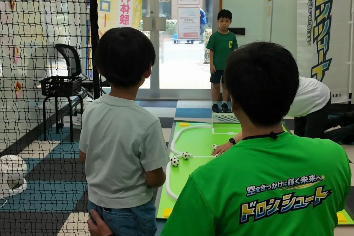 子どもドローン教室の体験会で、講師が子どもの隣に付き添いながらドローンシュートを教えている様子（東京都荒川区西尾久）